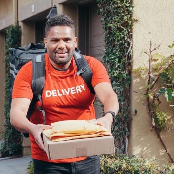 Friendly deliveryman in red delivering packages outdoors on a sunny day.