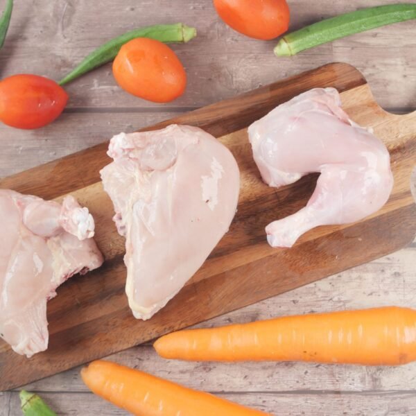 Overhead view of raw chicken, tomatoes, carrots, and okra on a chopping board.